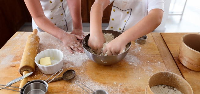 Two sets of children's hands preparing dough for baking.
