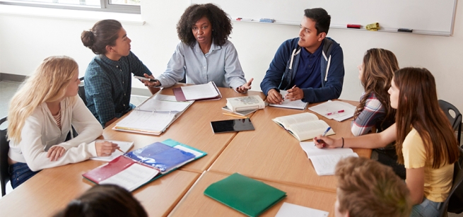 A group of teens sitting around a table having a discussion with notebooks and folders open.