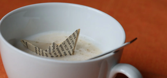 close up of an origami boat floating in a cup of coffee