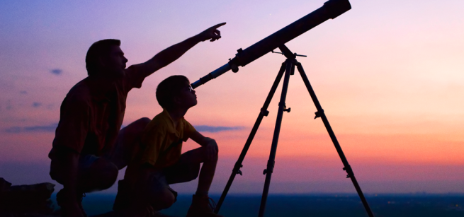 child and parent pointing up at the night sky with a telescope