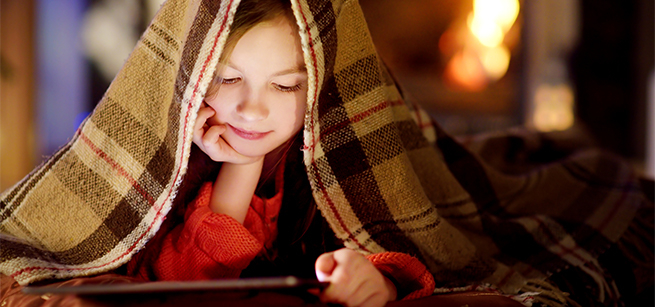 Girl under a blanket reads a tablet
