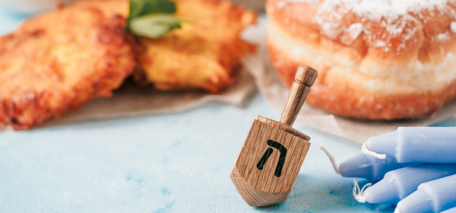 A dreidel beside blue candles, in front of fried snacks