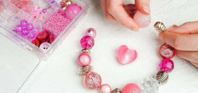 A person is making a bracelet using red and pink beads