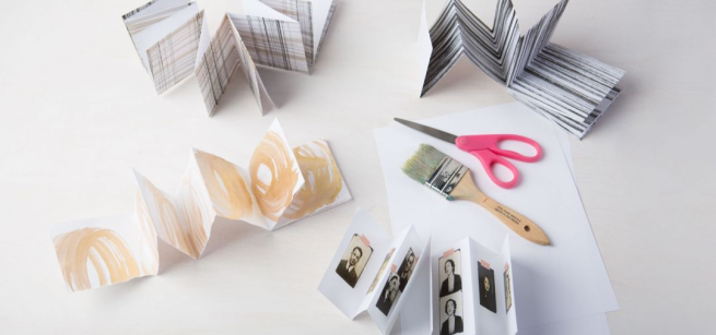 Several folded mini magazines (zines) are scattered throughout the table with a paintbrush and scissors shown. 