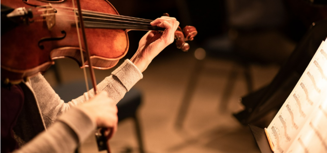 A person holding a violin while reading sheet music