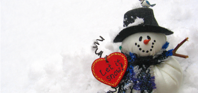 Snowman sitting in snow with a heart-shaped sign that says "let it snow"