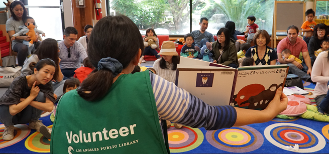 library volunteer holding a book and reading to children and parents