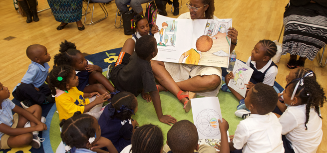 Woman holding an oversized picture book reading to a group of children.