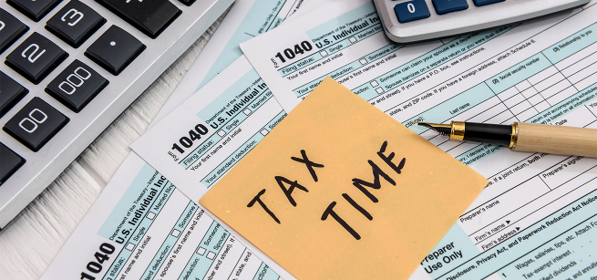 tax time written on a post-it note with tax paperwork, a pen and calculator in the background