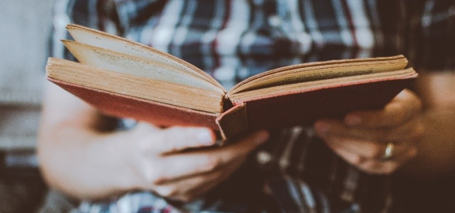 Man holding a book while wearing a plaid shirt