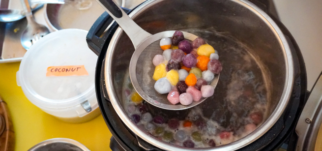 A ladle full of colorful dumplings over a large pot of dumplings.