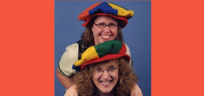 Two women standing together with colorful hats and stage costumes.