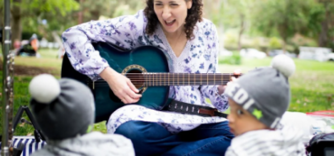 Woman playing a guitar to children.