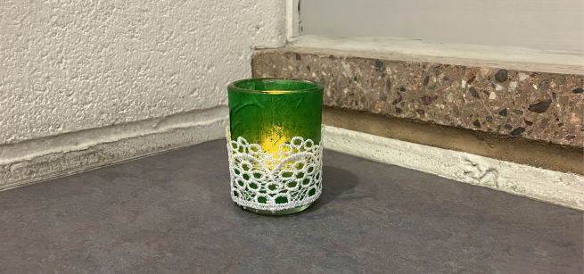 A green votive candle holder wrapped in lace with a lit candle inside