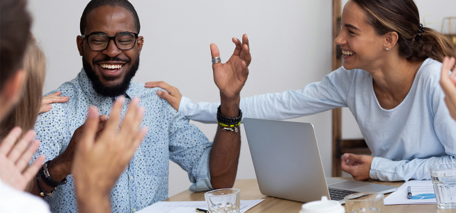 A group of adults sitting around a table with a laptop open.