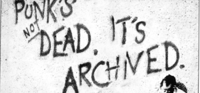 Black spray paint on a white wall "punks not dead. It's archived." A spray painted man sits in the bottom left corner.