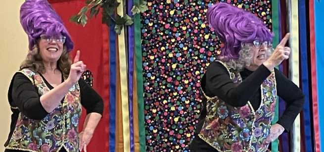 Two performers in purple beehive wigs and sparkly jackets wagging their finger at the audience