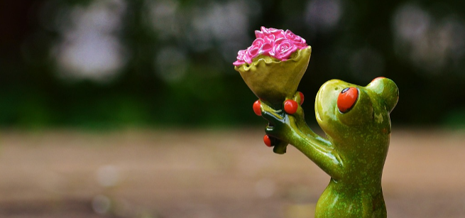 a ceramic frog offers a bouquet of pink flowers