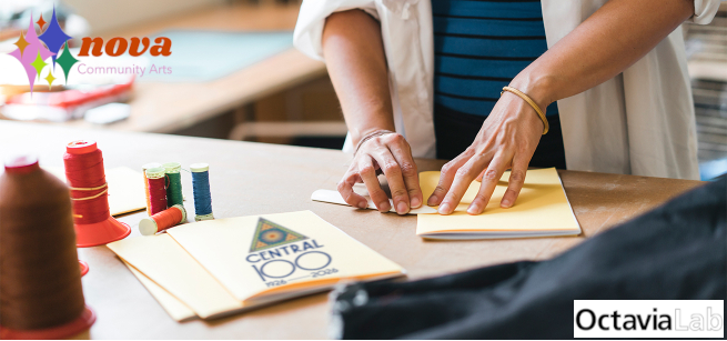 image of two hands folding a zine on a table with threads and art materials.