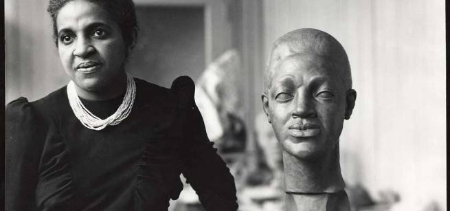 Selma Hortense Burke standing beside a bust in her studio, black and white photo