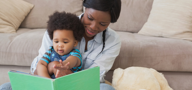 A mother reads from a book to the baby sitting in her lap.