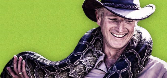 Man wearing a hat with a very large snake draped around his neck.