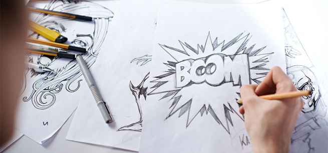 A person’s hand is shown drawing the word boom in bold letters with a pencil on a blank sheet of white paper
