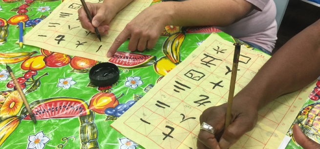 three hands write chinese calligraphy on a table with a colorful tablecloth