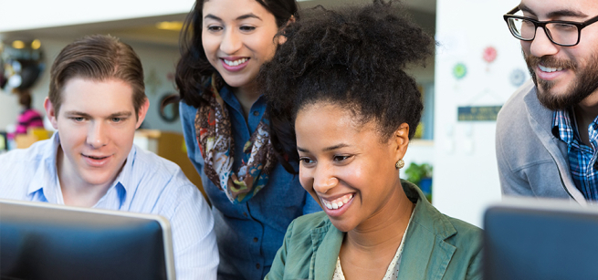 four adults looking at a computer, smiling 