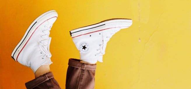 feet wearing white converse pointing up in front of a yellow wall