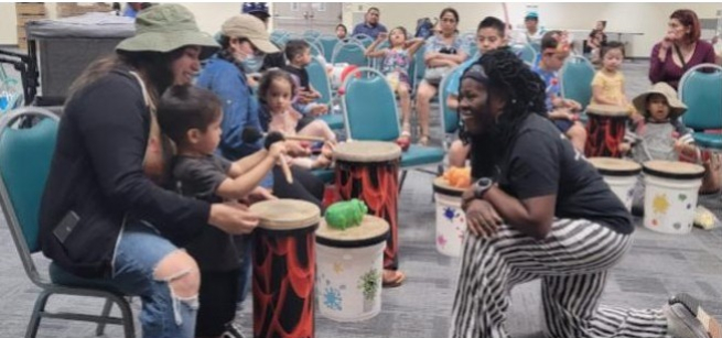 Woman kneeling in front of a mother and child playing a drum