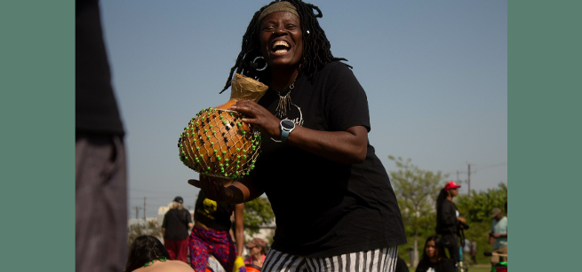 Diana Lynn, musician, plays a small handheld drum while smiling and dancing.