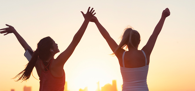 Two women exercising outside with arms raised. 