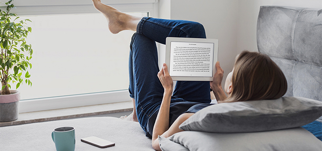 A girl reads on her tablet by a sunny window