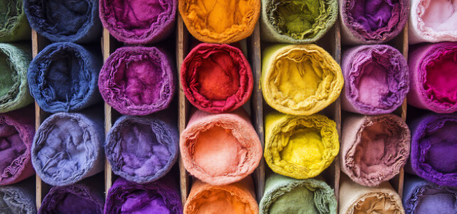 An assortment of tightly rolled fabric bolts in a vibrant spectrum of colors.