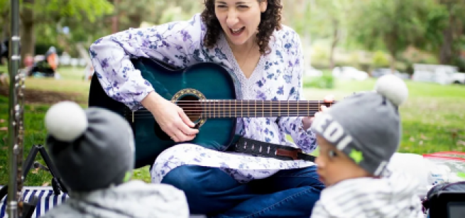 a woman playing a guitar to children