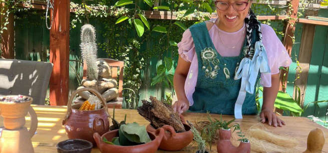 Creator Taty Hernandez stands at a table behind several of her ceramic creations