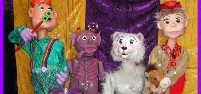 Four marionettes, l to r: red-hatted white human-type in green with bubble wand, purple alien, white furry bear, blonde white human-type in tan and red with brown hobby horse 