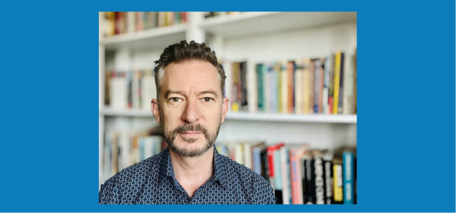 A photograph of Martin Jago wearing a dark blue collared shirt pictured in front of a bookcase.