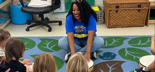 performer Kimberly Stewart sitting cross legged on a rug with some small children