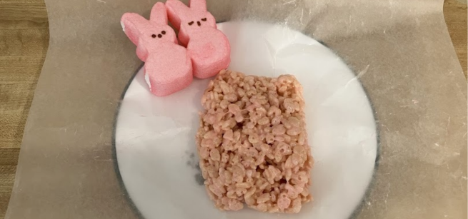 A pink Rice Krispies treat and two pink Bunny Peeps on waxed paper on a plate