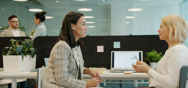 Two adults in a business setting sitting in chairs, facing each other, having a conversation