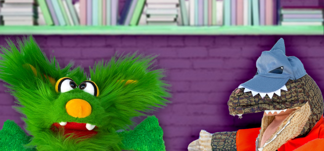 The image shows two puppets in the library. The first puppet is Ellie, a green fluffy puppet, who is confronting the Library Bandit, a masked dinosaur puppet, for stealing her books.