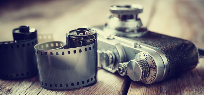Close up photo of a camera and two rolls of 35mm film on a wooden surface.