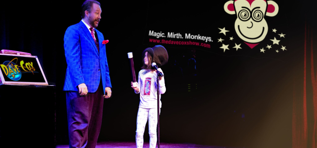 an adult man magician stands with a child in a top hat on stage