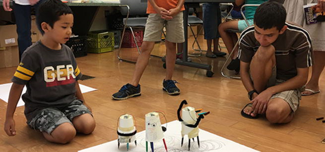 Children watch as their Art Bots bounce around on marker legs, making their own "art".