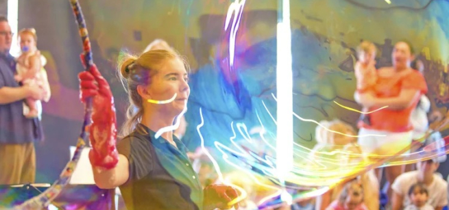 Instructor making a big bubble with a big hoop while families watch.