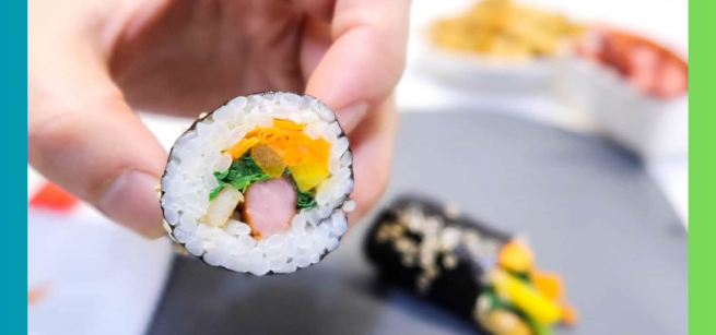 A hand grabbing a slice of mini kimbap and a out of focus roll in the background