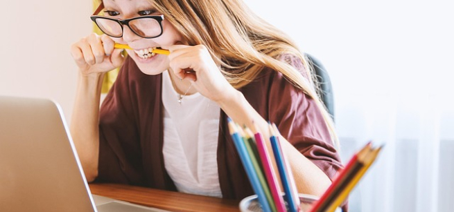 A picture of a woman at a laptop, biting a pencil.