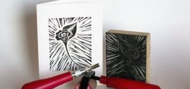 A black and white printed card, a linoleum block, and a red handled carving tool, and a red handled brayer.